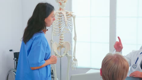 female nurse demonstrating on skeleton in front of medical surgeons