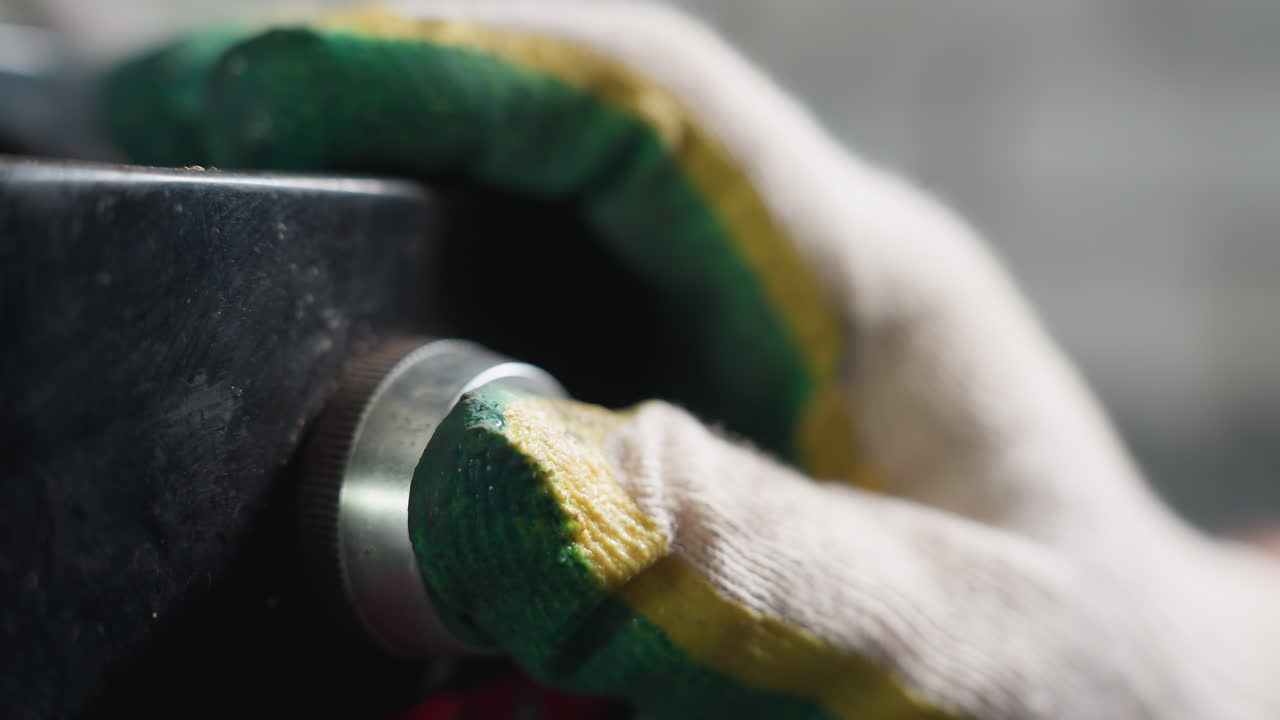 primer plano extremo de la mano con guante de un mecánico presionando un botón en la maquinaria industrial, centrándose en la textura del guante y la superficie metálica