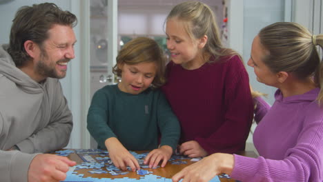 family with children sitting around table at home doing jigsaw puzzle together