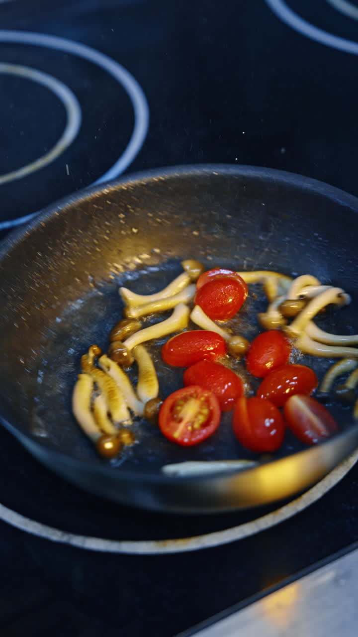 Some mushrooms are fried on the frying pan. Fresh tomatoes are added to fry. Close up. Vertical video.