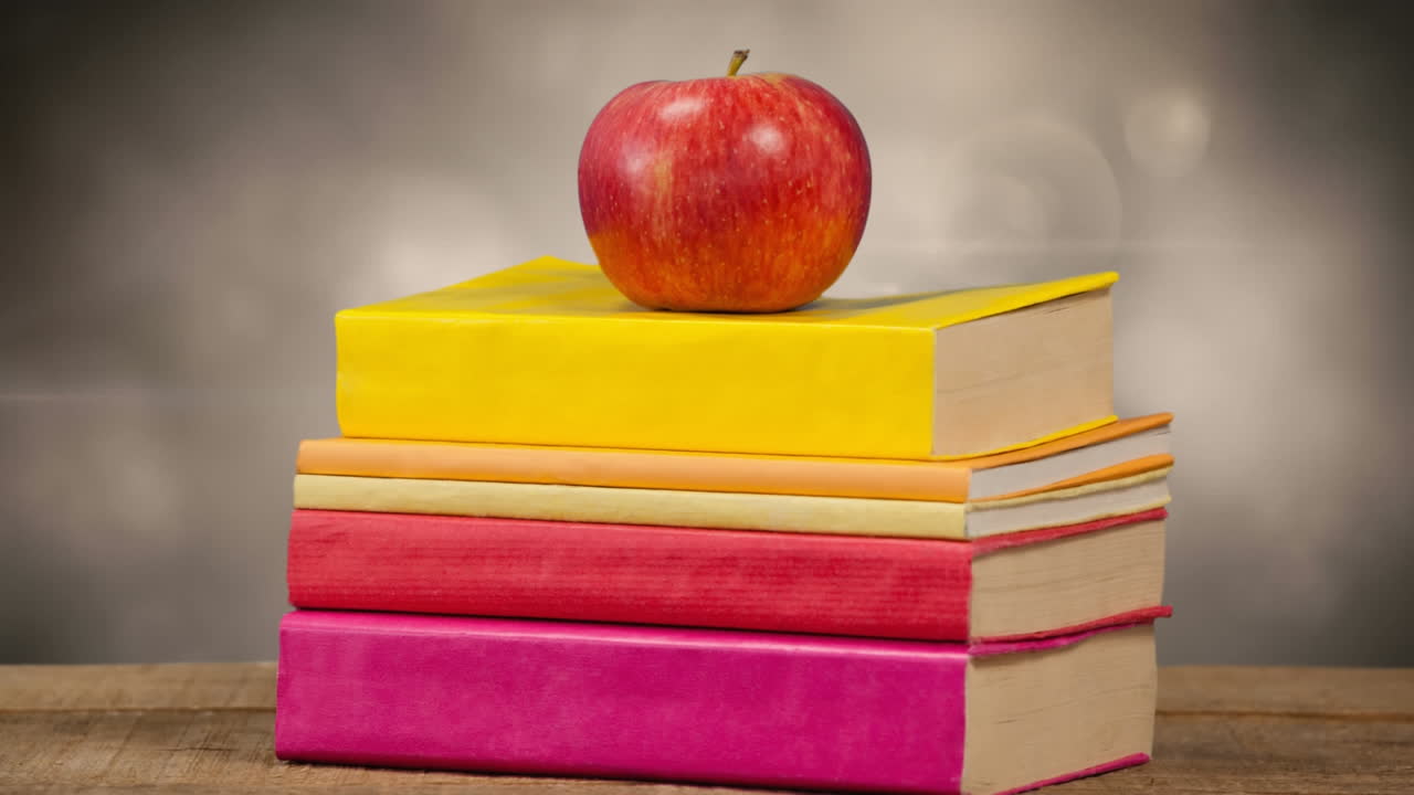Animation of stack of books with red apple on top over glowing lights