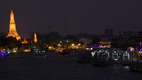colorful boats glide along the chao phraya river at night, with bangkok's illuminated skyline in the background