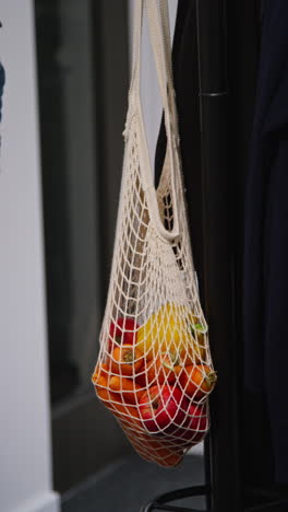 vertical video of woman getting home from food shopping hanging bag of fresh vegetables on coat stand