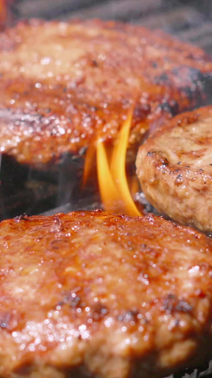 Vertical Video Flames Licking Juicy Sizzling Beef Burgers on BBQ Grill. Perfect for food commercials, summer eating social media content. 4K.