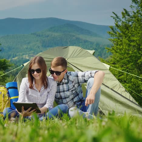 a young couple is using a laptop while camping with a tent