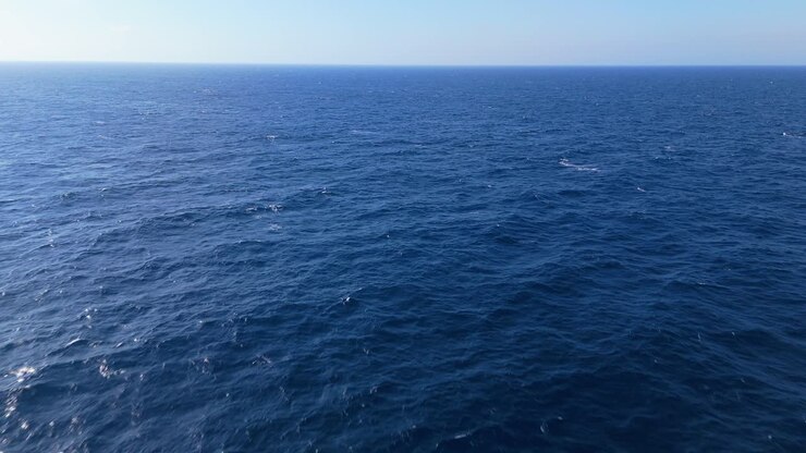 Calma superficie blu dell'oceano con leggere increspature e luce solare delicata, perfetta per sfondi sereni.