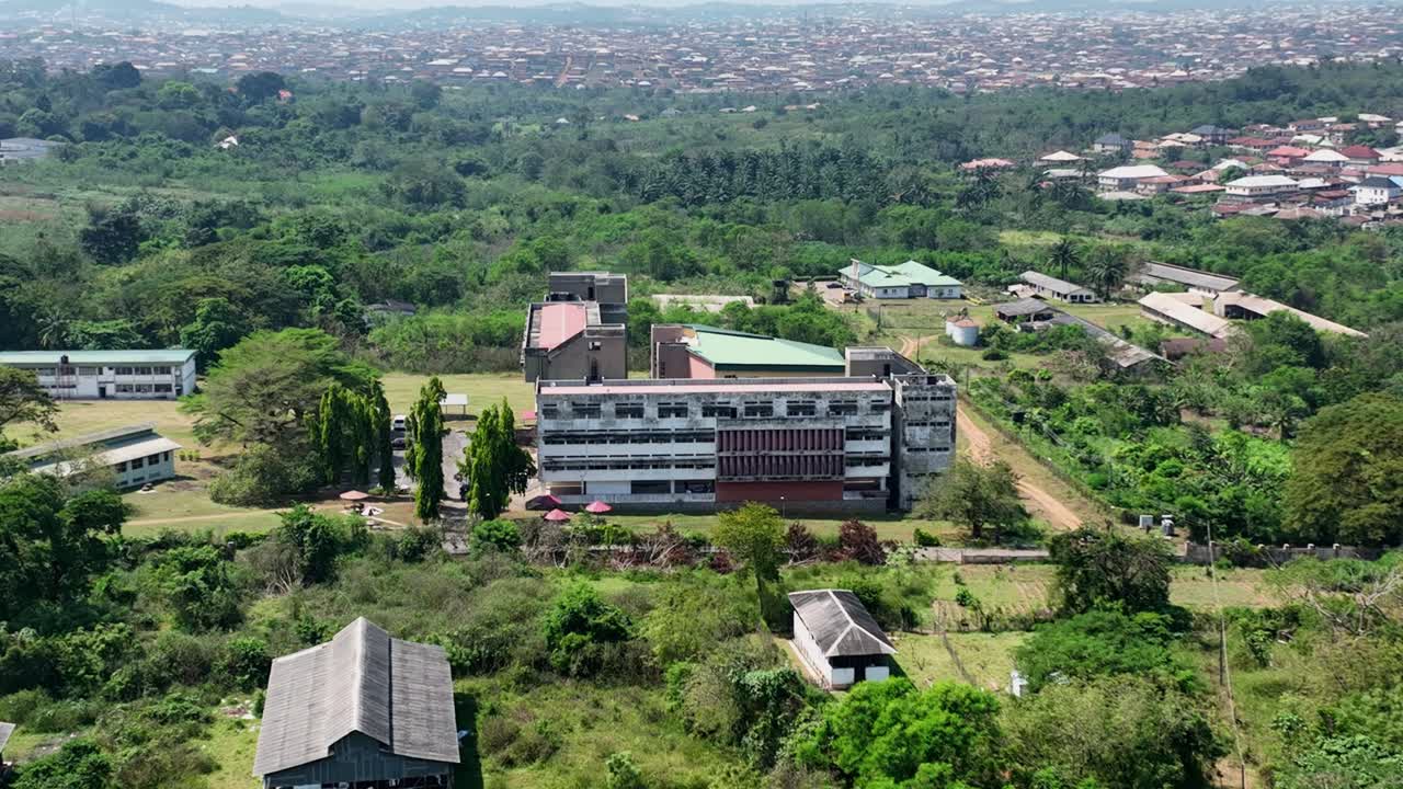Udara - Bidikan lebar miring ke depan sebuah bangunan di kampus universitas yang dikelilingi pepohonan.