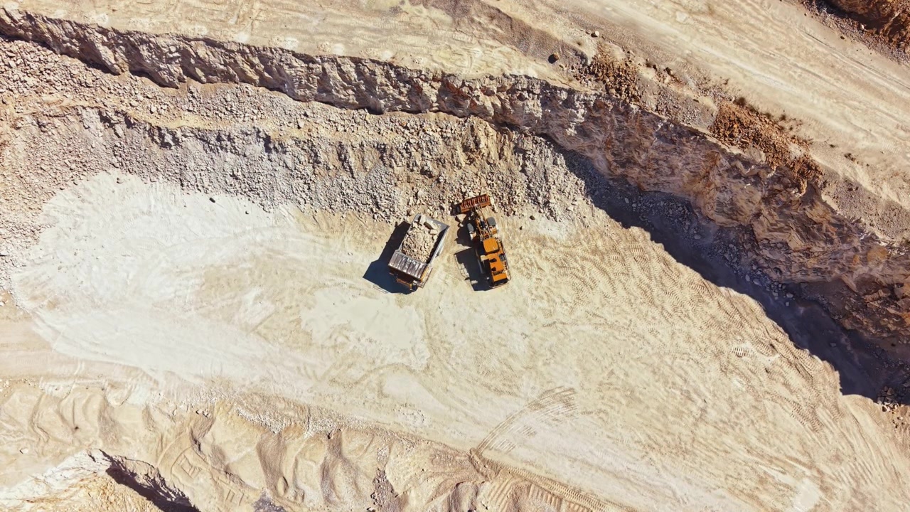 Quarry work happens with large machines and equipment at a mining site during a sunny day in an open area