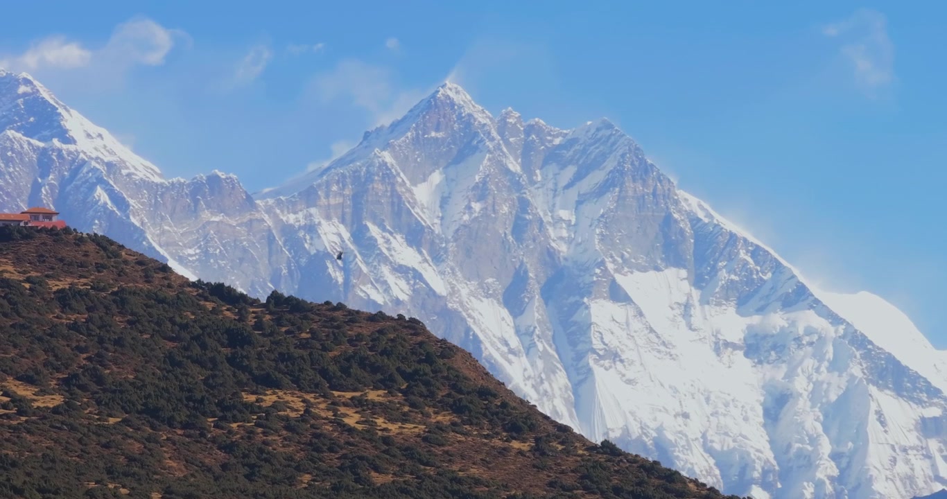 Regione dell'Everest, Nepal. Ripresa verticale con gru che si alza oltre una cresta montuosa rocciosa per rivelare un elicottero che vola contro le maestose vette del Monte Everest e del Lhotse