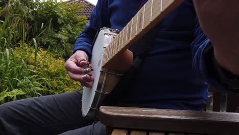 Man-relaxing-on-garden-seat-finger-picking-a-tune-on-the-banjo