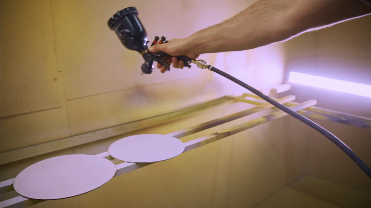 Close-up of Hand Spray Painting Round Objects in Workshop