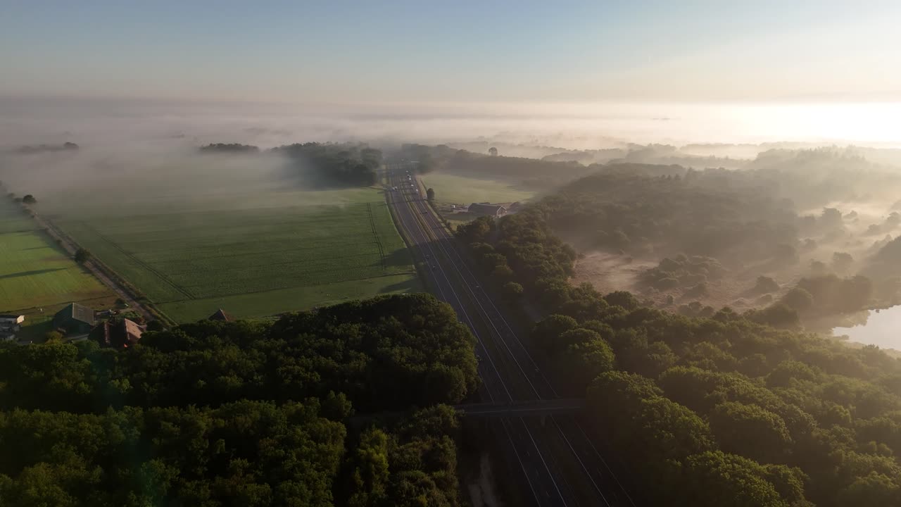 Aerial view of a foggy morning landscape with a highway, forests, and fields