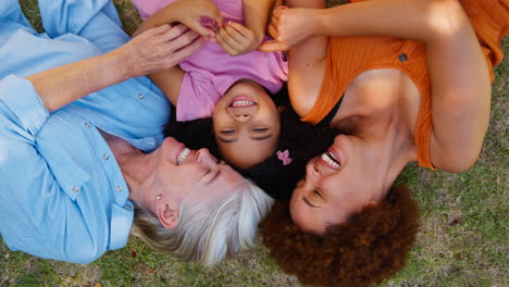 retrato aéreo de una familia de mujeres de varias generaciones acostadas en la hierba cosquilleando a su nieta
