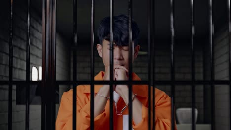 primer plano de prisionero masculino asiático con esposas reza por algo mientras está de pie en la cárcel