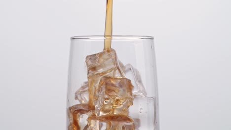cerca de cola fresca que se vierte en el vaso con cubos de hielo en fondo blanco