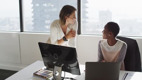 Two-diverse-female-colleagues-looking-at-laptop-and-discussing-in-office