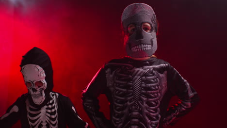 fotografía de estudio de niños vestidos con trajes de esqueleto haciendo trucos o golosinas en halloween bailando frente a la luz de fondo de humo rojo 1