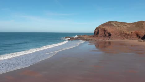 Toma-Aérea-Sobre-Una-Playa-De-Arena-Con-Reflejo-Durante-La-Marea-Baja,-Plemont-Bay,-Jersey,-Islas-Del-Canal,-4k