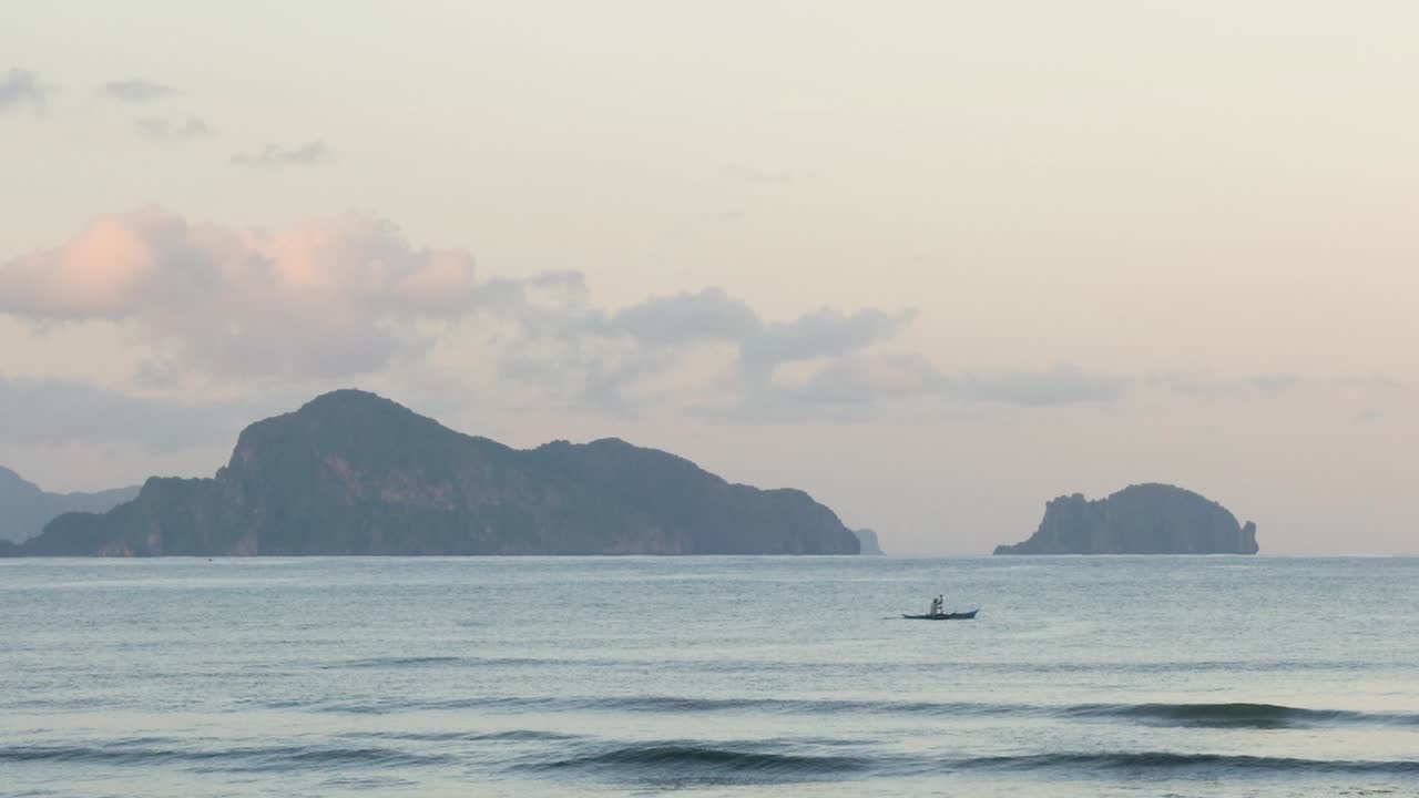 해변에서 본 해질녘에 석회암 절벽 앞에서 보트에 노를 젓는 남자의 슬로우 모션 샷