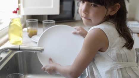 una niña seria lavando platos por sí misma.