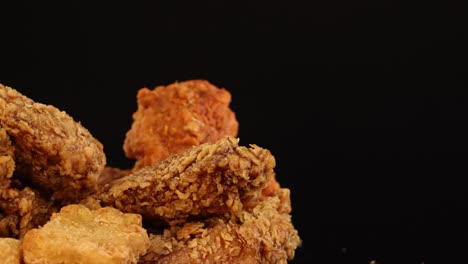 assorted fried chicken breasts and thighs rotate against a black background, highlighting golden, crispy breading and spicy seasoning under studio lighting
