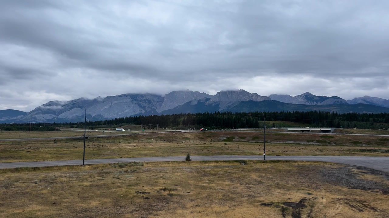 Wide view of Alberta plains with distant mountains under cloudy sky, overcast day