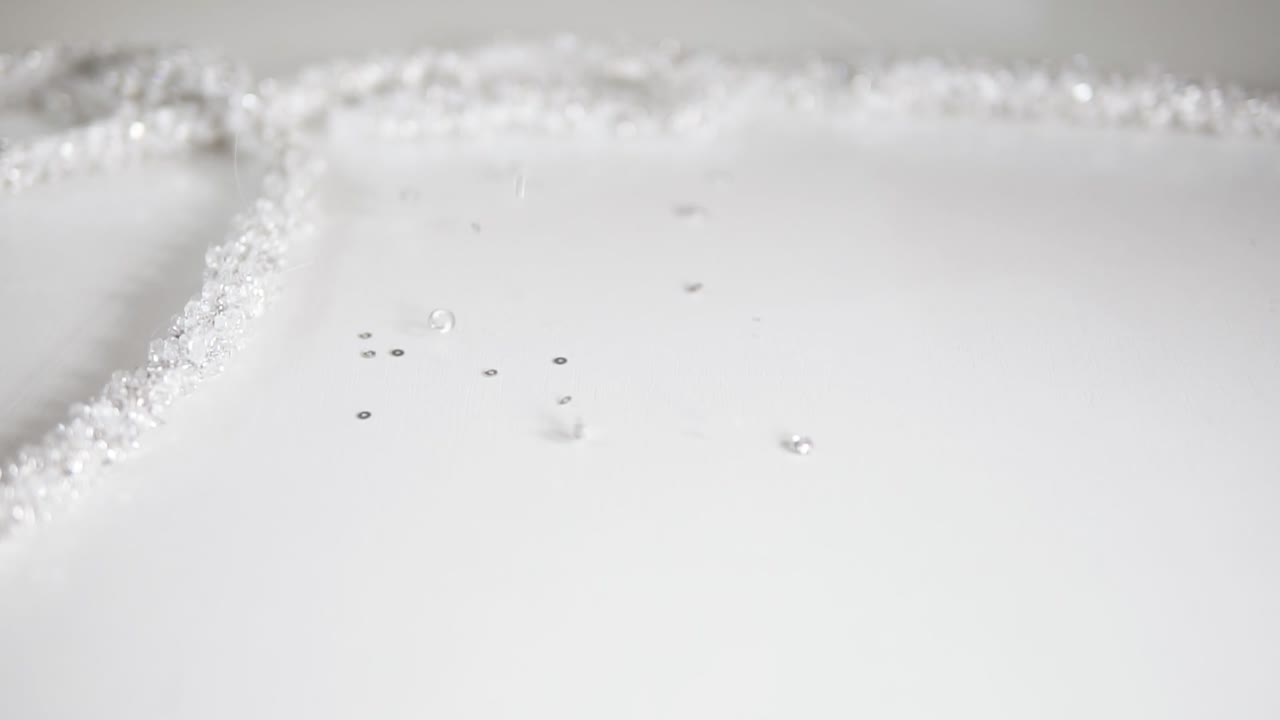 멋진 질감의  ⁇ 색 웨딩 드레스의 스테디캠 영상으로 구슬과 장식적인 돌이 패턴에  ⁇ 아져 있습니다. 떨어지는 구슬의 클로즈업 뷰. 느린 움직임