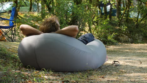 hombre relajándose en una bolsa de aire en un campamento.