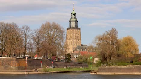 fluffy clouds passing by over the walburgiskerk cathedral tower seen from the other side of the river ijssel passing the cityscape quay of the medieval town zutphen in the netherlands