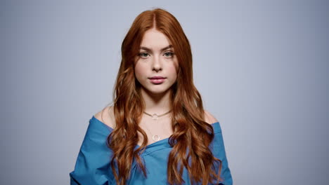 Relaxed-woman-posing-on-gray-background.-Redhead-girl-looking-camera-in-studio