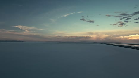 aerial view of bonneville salt flats in utah with the sun on the horizon and sparse clouds