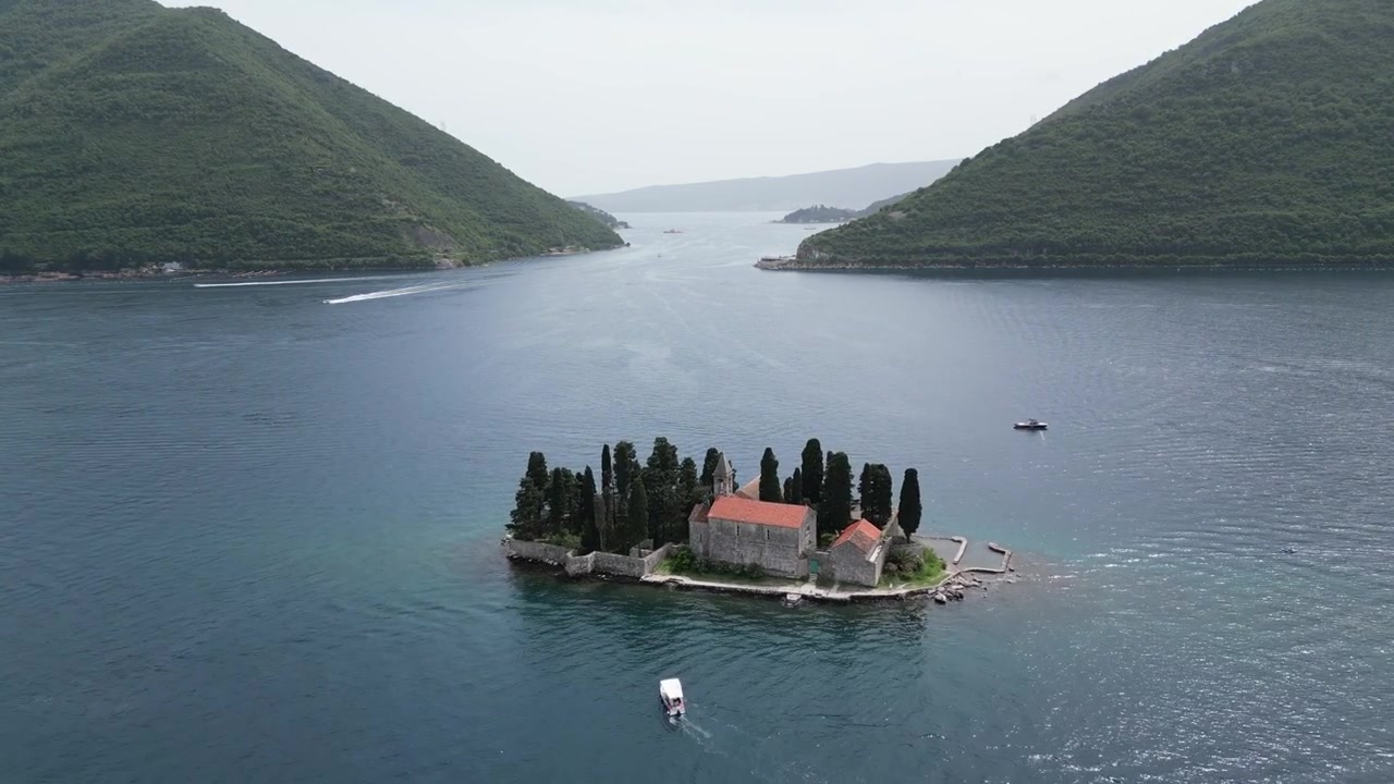 Karadağ, Kotor Körfezi'nde sakin mavi sularla çevrili, tarihi bir kilise, selvi ağaçları ve teknelerin yer aldığı Kayalıklar Meryem Ana Adası'nın havadan drone görüntüsü