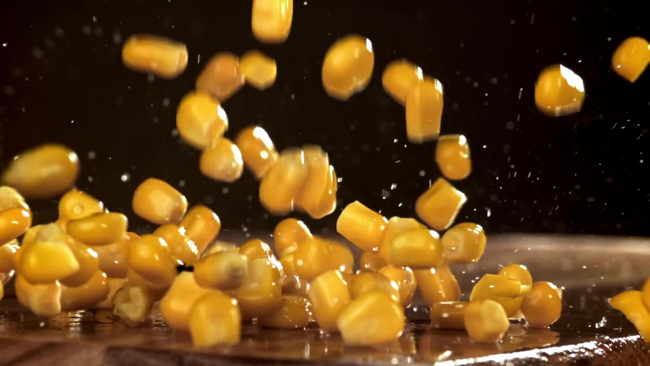 Friske majskorn falder og sprøjter på en våd overflade i slow motion