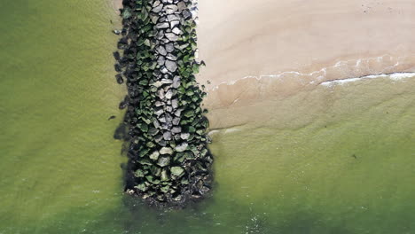 a top down drone view of a stone jetty as the ocean waves gently crash onto the shore