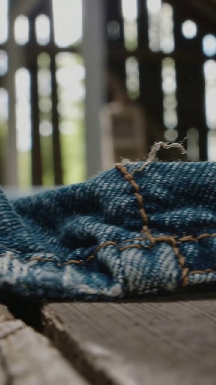 Video verticale: Spostamento della telecamera che rivela una cucitura di jeans blu con impunture arancioni e fibre su una tavola.