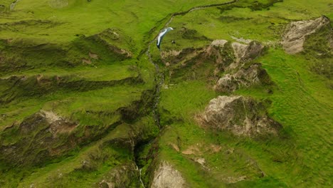 Parapente-Sigue-Un-Arroyo-De-Montaña-A-Través-De-Un-Exuberante-Terreno-Montañoso,-Aéreo