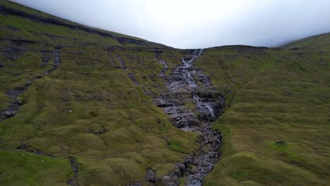 aerial rising shot on a flowing river over green and foggy volcanic landscape in streymoy island, faroe islands