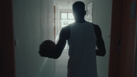 black man walking along corridor and tossing basketball