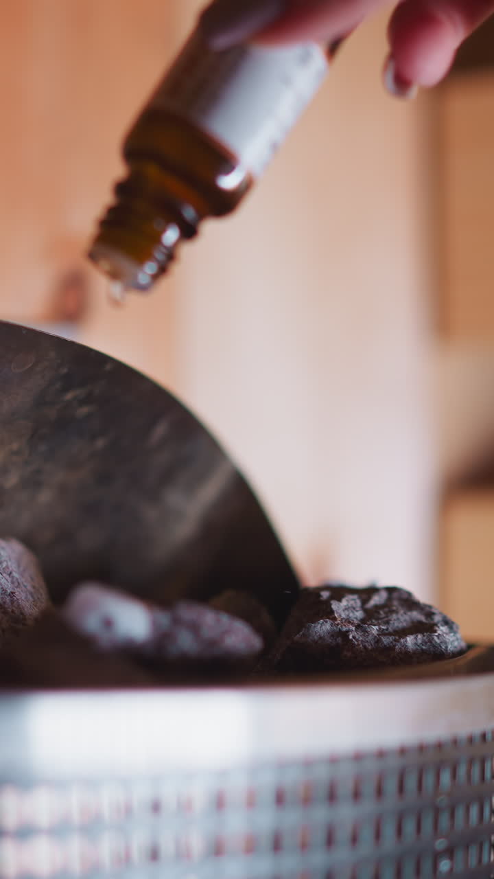 Woman drops essential oil on rocks in sauna. Process cultivates soothing atmosphere and enhances positive health benefits from hummum, Positive health impact