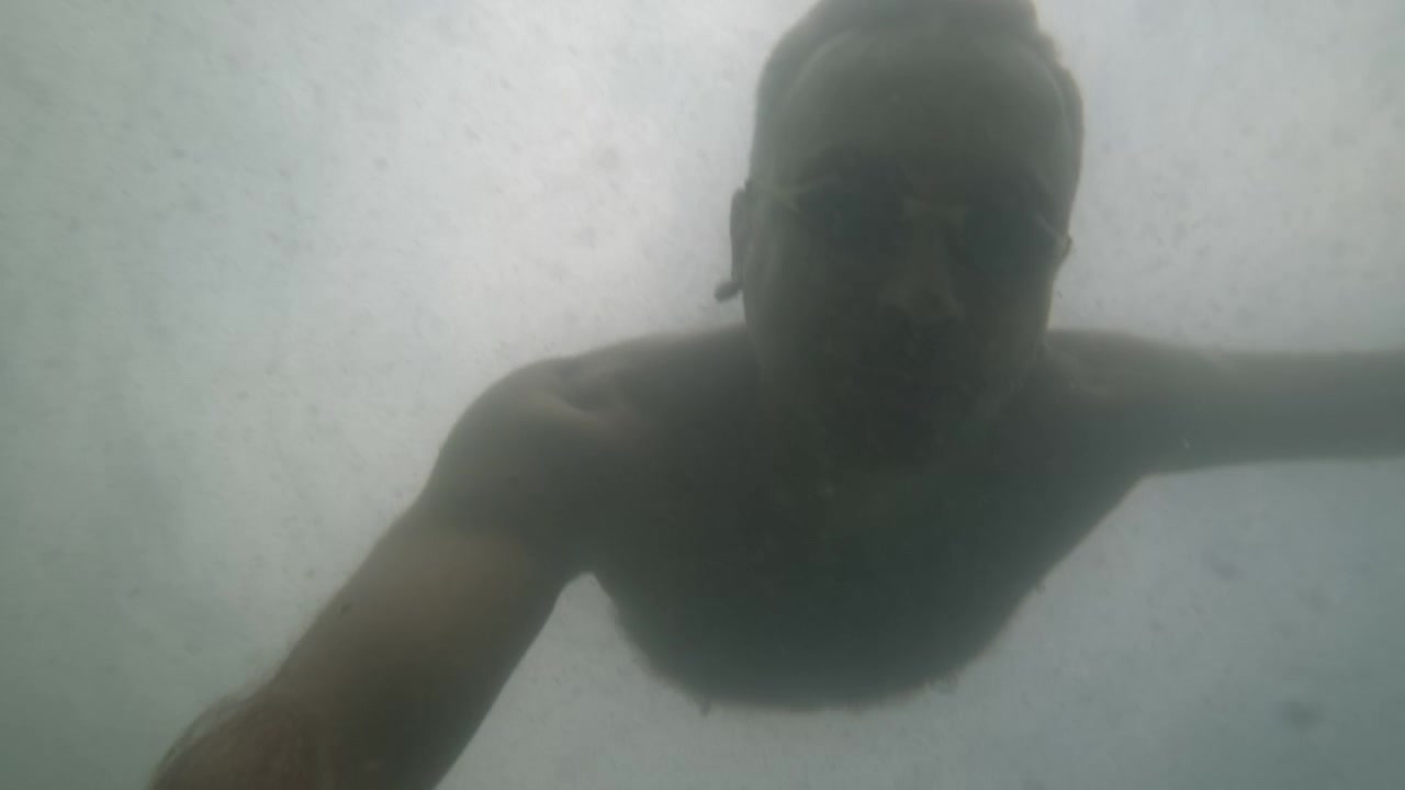 Slowmotion undervandsnærbillede af en mand med svømmebriller, mens sollys filtrerer gennem havet, Côte d'Azur, Frankrig
