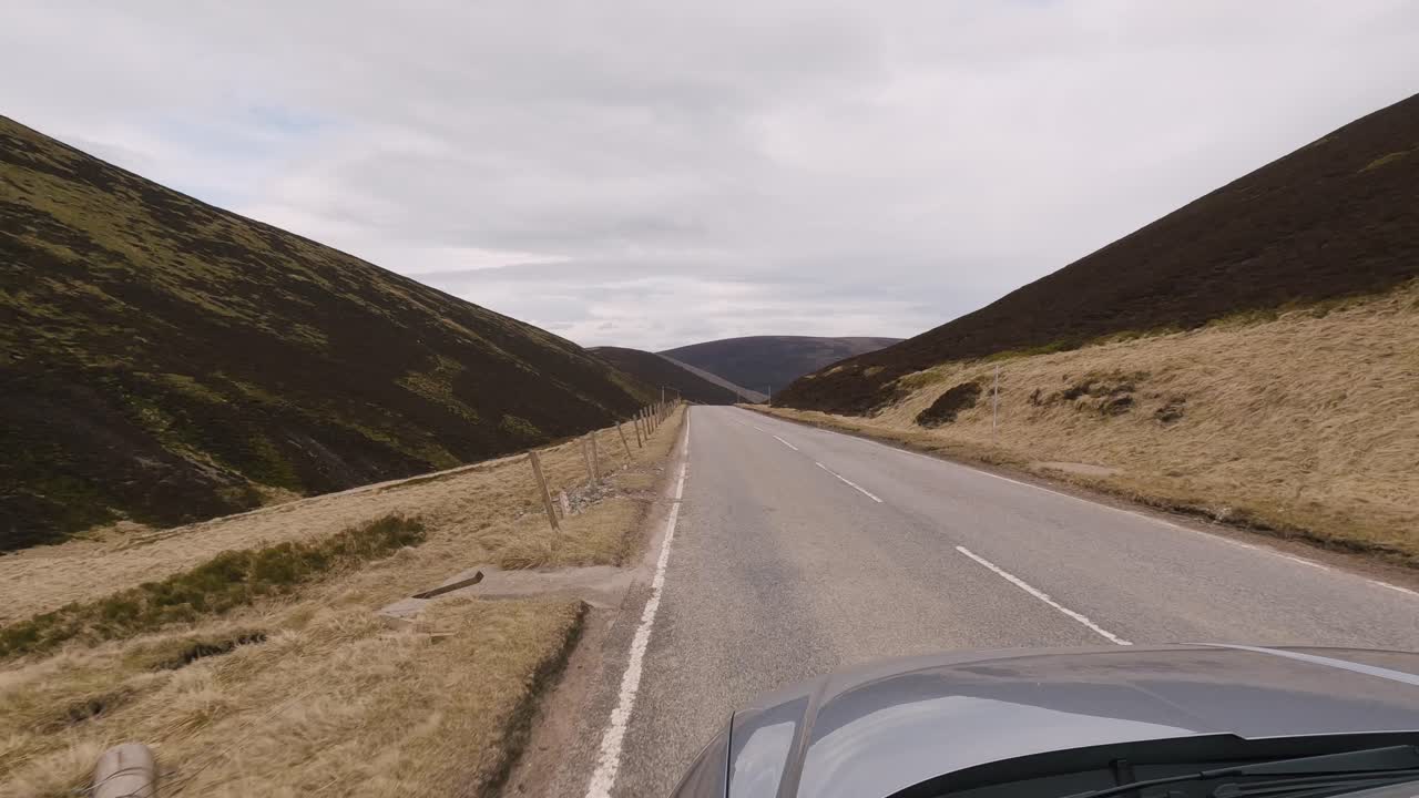 Passing landscapes of the Scottish Highlands through the window of a grey car on a cloudy day