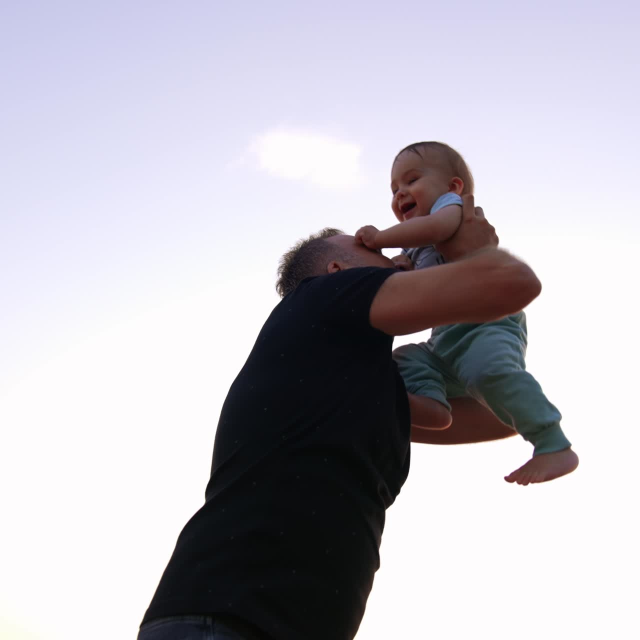 Padre affettuoso che solleva il figlio in aria e gli bacia la pancia. Papà che lancia in aria il suo bambino. Inquadratura dal basso