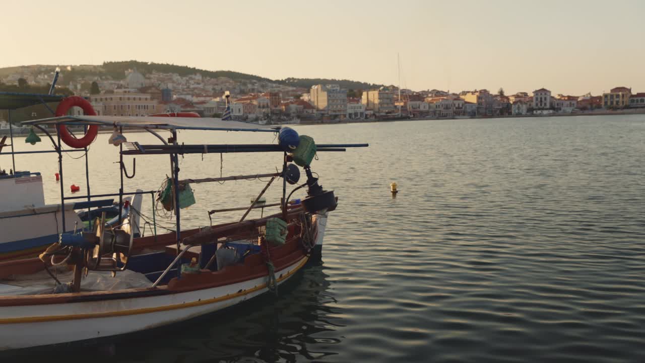 Una tradizionale barca da pesca in legno che galleggia dolcemente nelle acque calme del porto di Mitilene, con lo sfondo della città e delle colline, luce solare all'ora d'oro