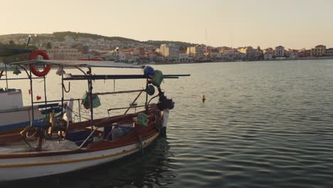 a traditional wooden fishing boat gently floating in the calm waters of mitylene port, with the backdrop of the city and hills, sunlight at golden hour.
