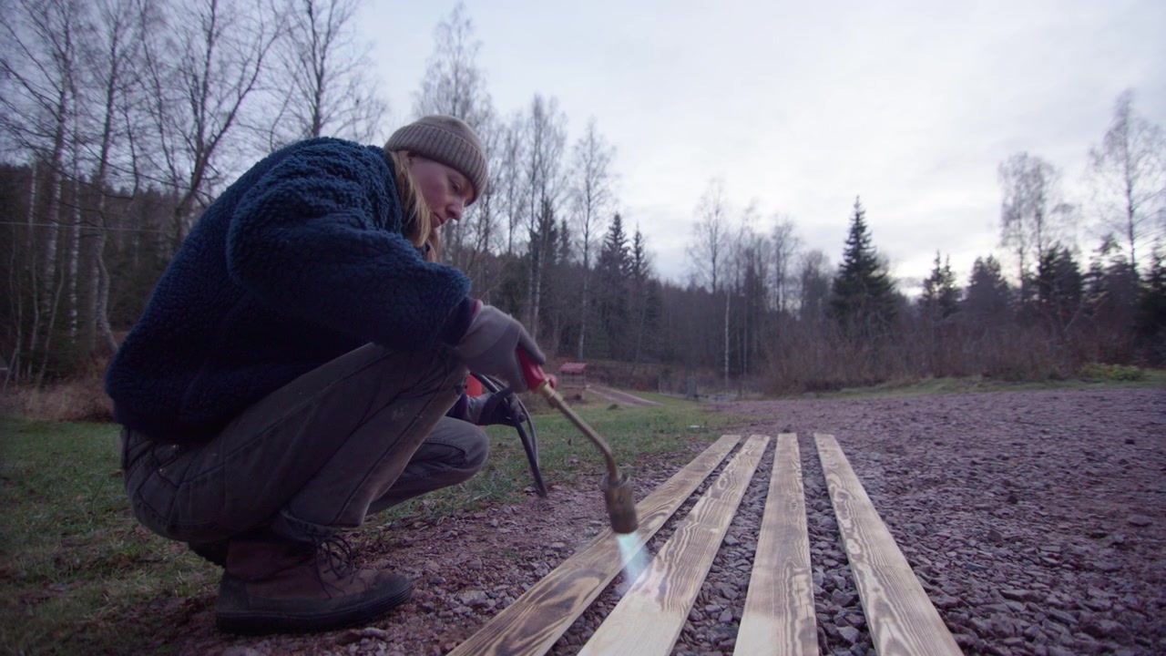 Handykvinne bruker blåselampe for å brenne planker med tradisjonell teknikk, glidende opptak.