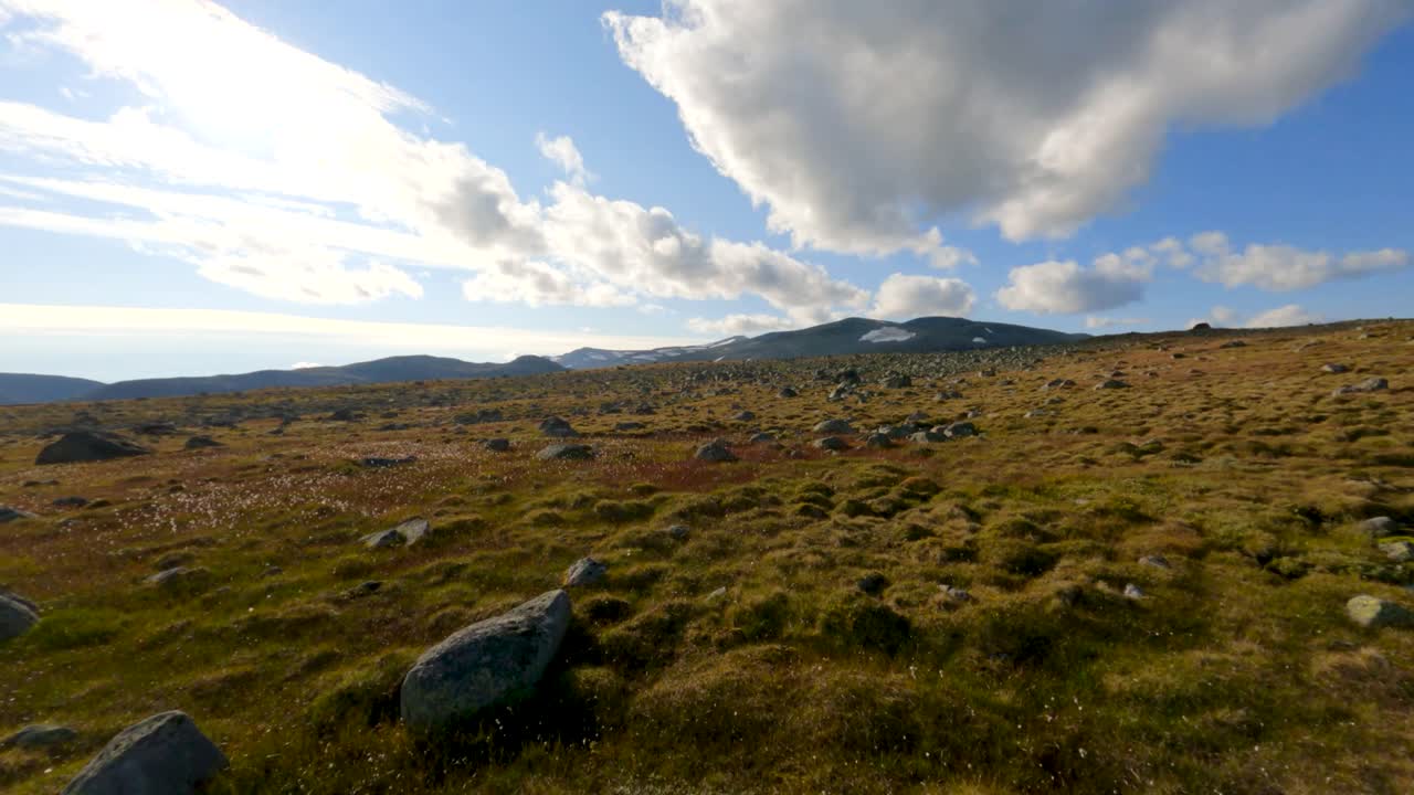 un impresionante paisaje montañoso en el municipio de øystre slidre, noruega, con extensos campos de hierba, terreno rocoso y un cielo azul brillante con nubes dispersas