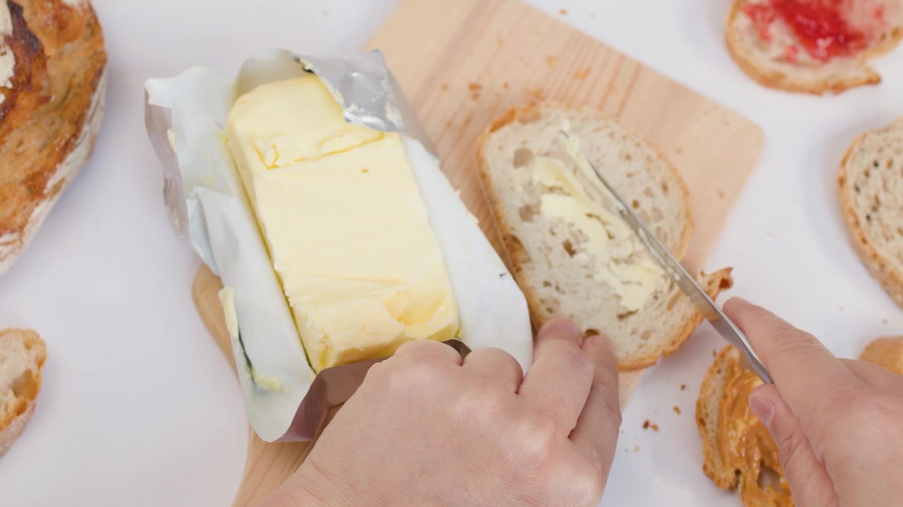 Ripresa dall'alto di mani che tagliano il burro e lo spalmano su fette di pane fresco a lievitazione naturale