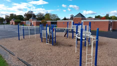 playground with blue and white equipment on wood chips, next to a school and basketball court