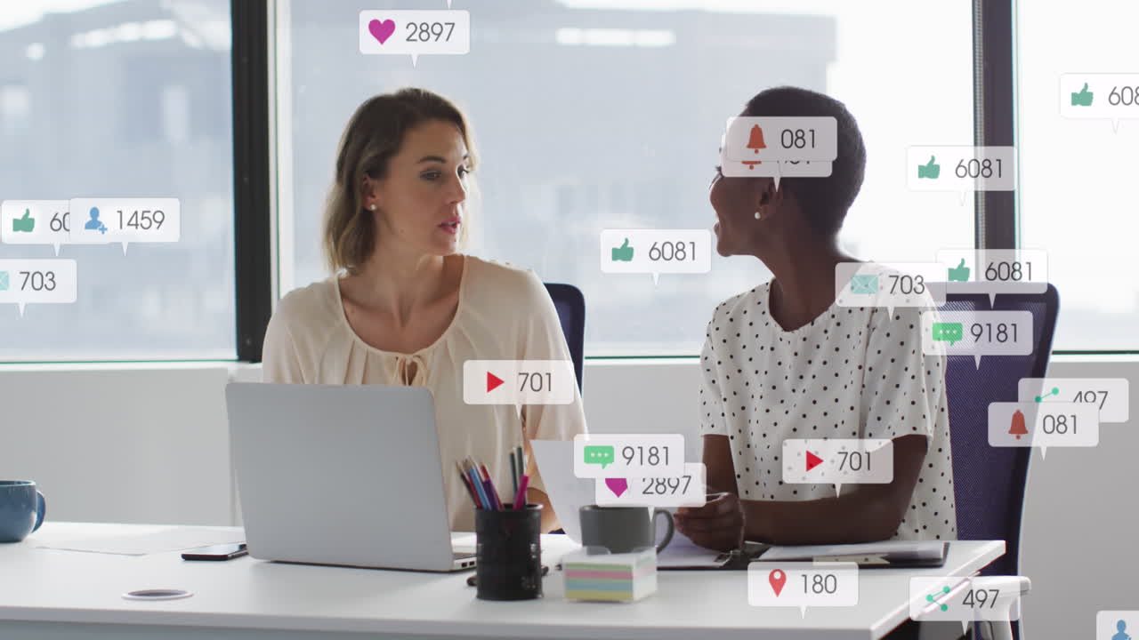 Animation of social media icons against two diverse women discussing over a document at office