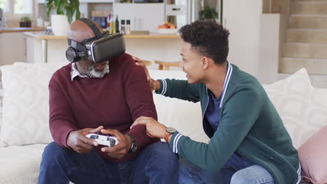 Glücklicher-Afroamerikanischer-Vater-Mit-VR-Headset-Und-Gamepad-Mit-Erwachsenem-Sohn-Zu-Hause,-Zeitlupe